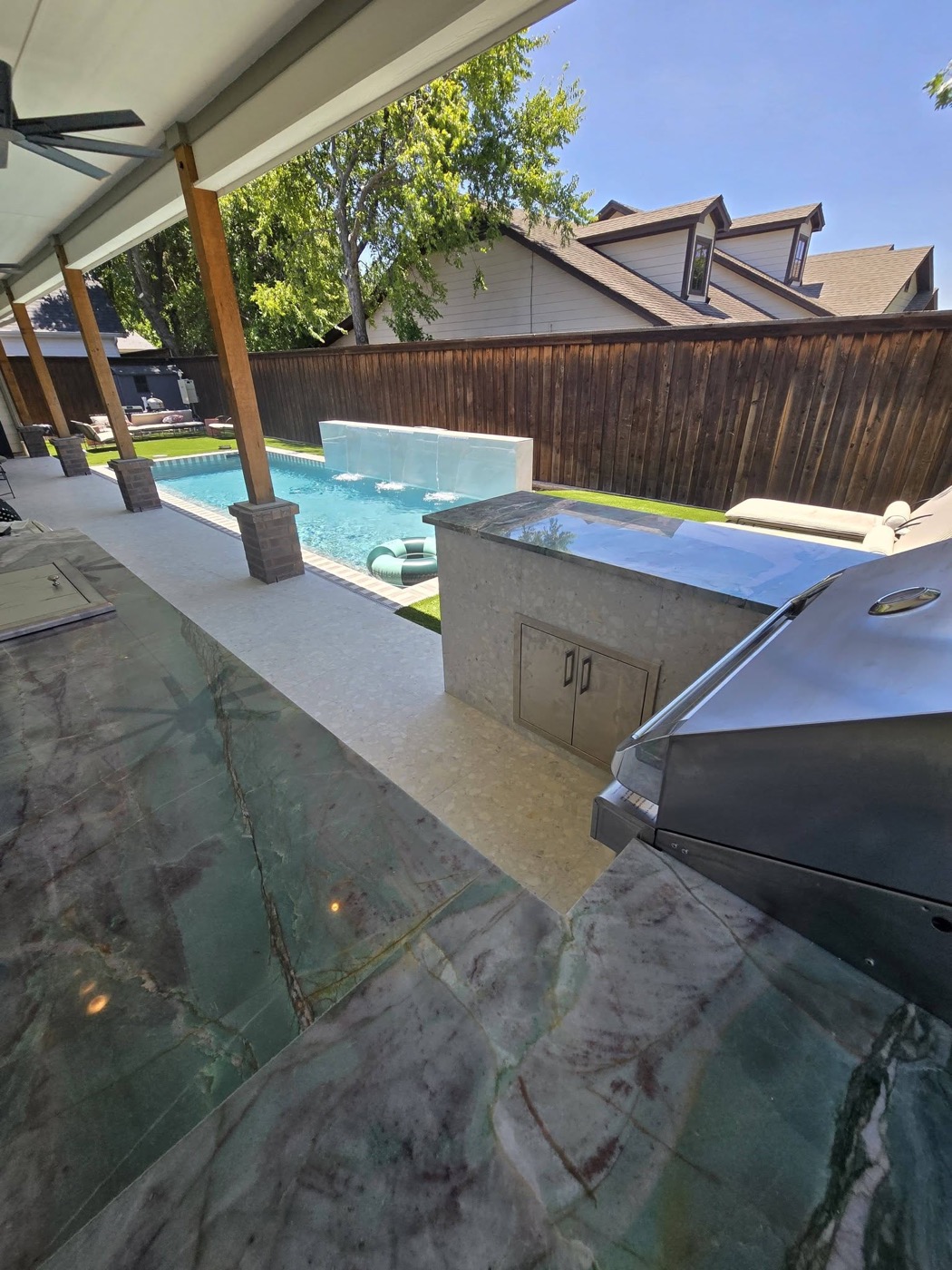 Outdoor kitchen island with built-in grill and granite counter beside a pool