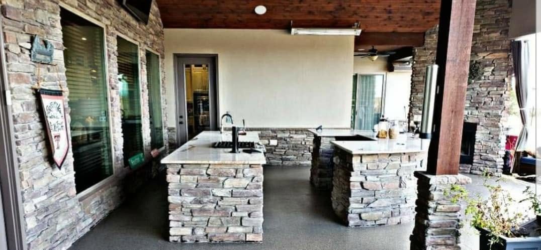 Stacked stone outdoor kitchen with twin islands, stone counters, and a sink