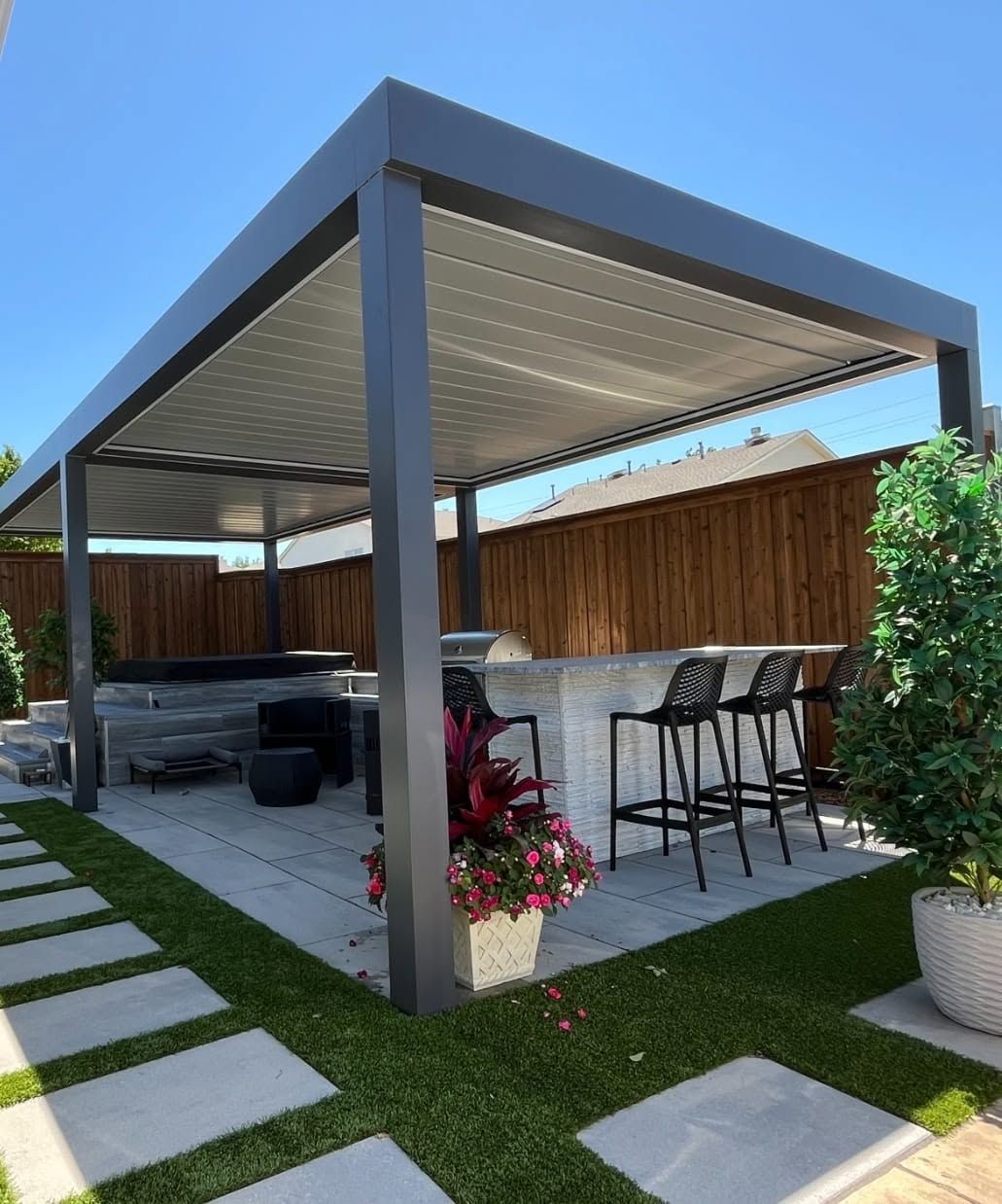 Modern louvered pergola over a stone bar, grill, and spa with turf and pavers
