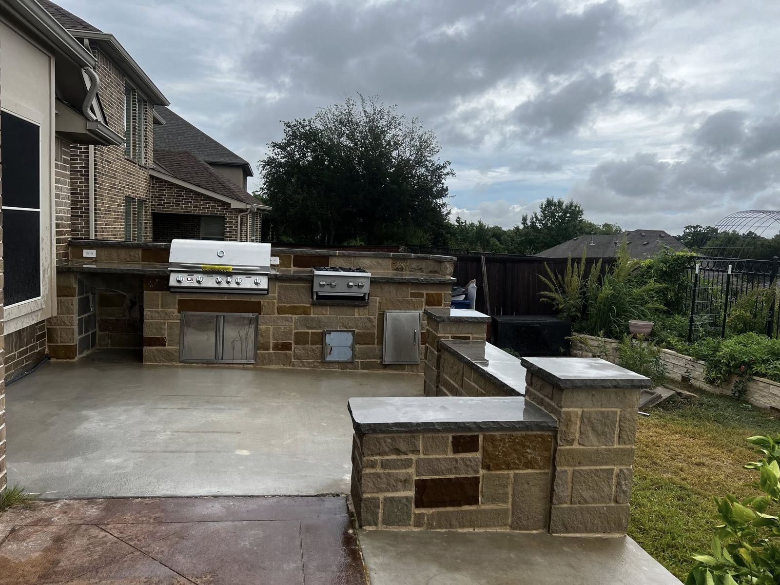 Large stone grill island with double grills on a stamped concrete patio