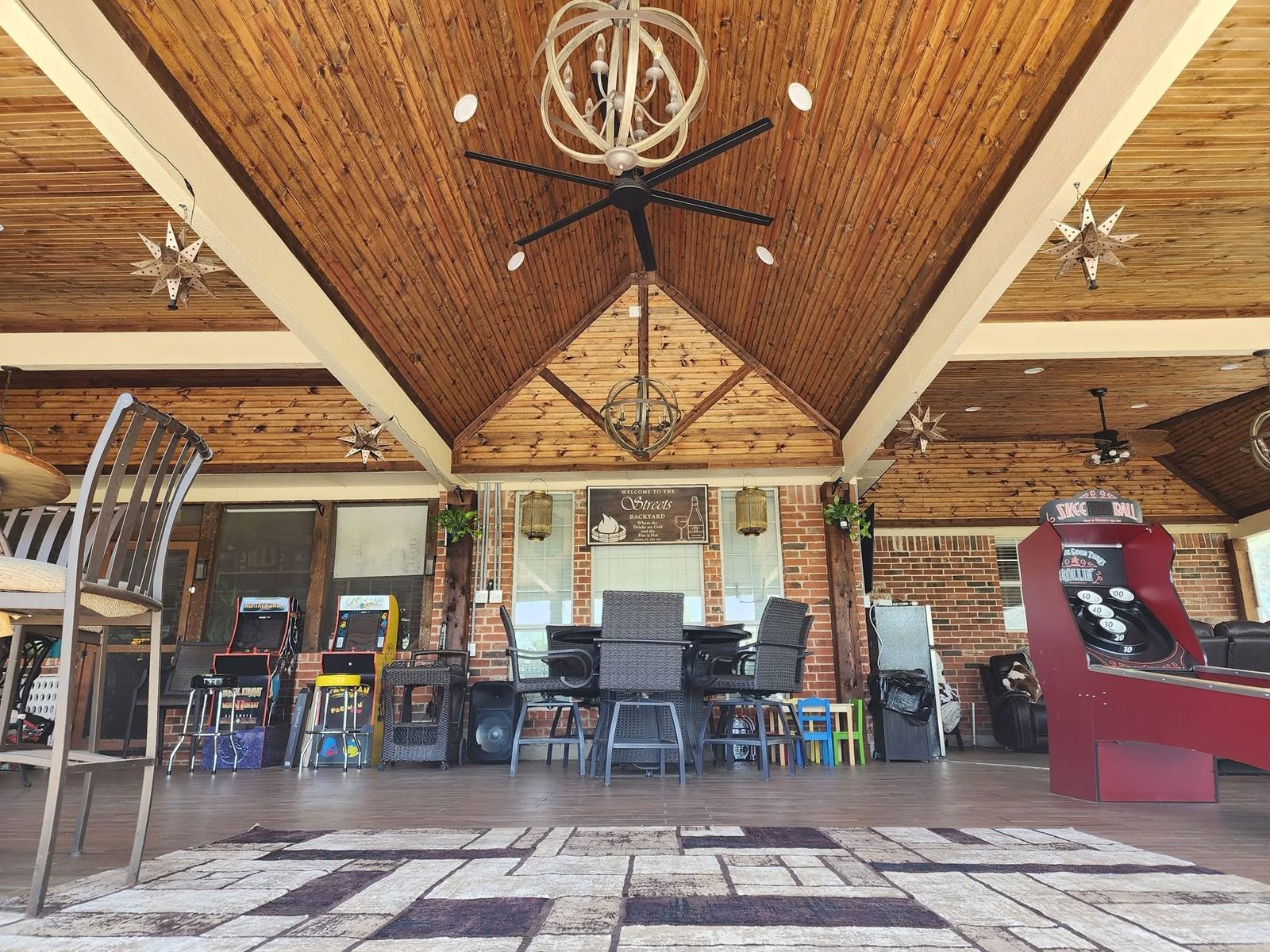 Covered outdoor room with vaulted stained wood ceiling, chandelier, and bar seating