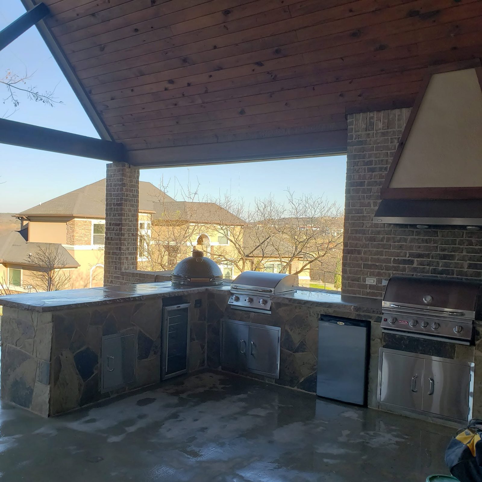 L shaped stone outdoor kitchen with a Big Green Egg, twin grills, and a brick hood