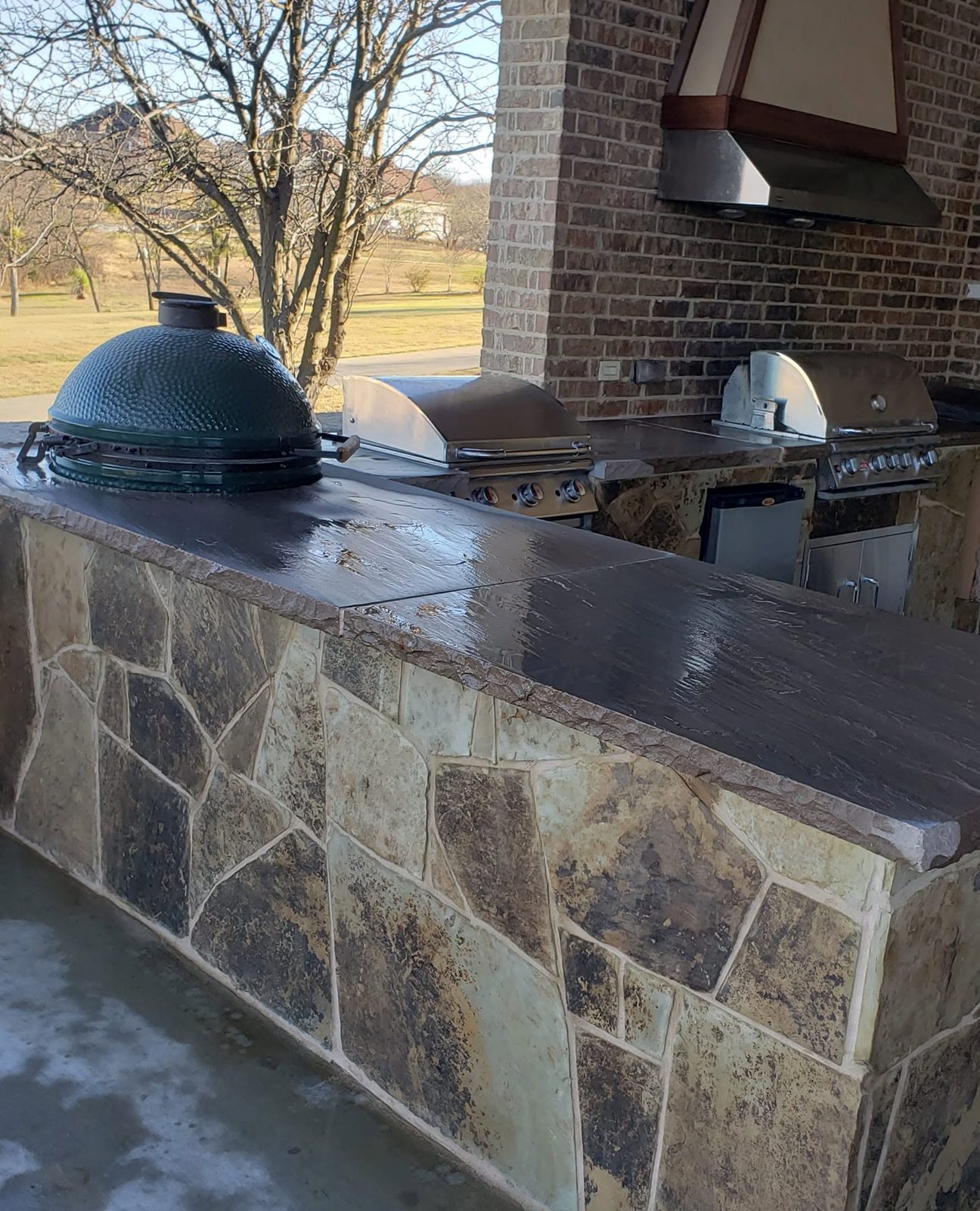 Stone bar with a Big Green Egg and built in grills under a brick hood